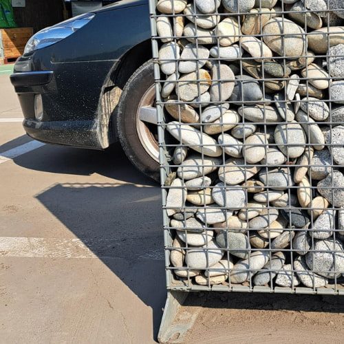 Close-up van een gevulde steenkorf met Beach Pebbles Flat Gray 50/100 in een naast een geparkeerde auto."